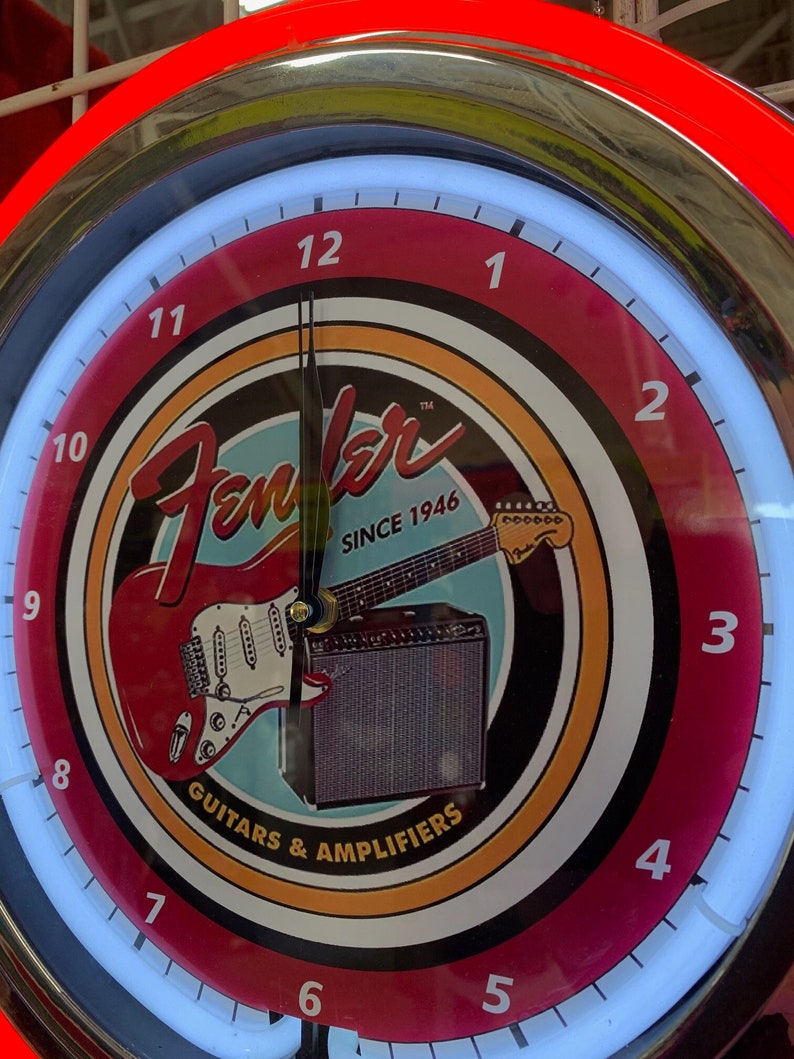 May include: A circular clock with a red and white face, displaying the Fender logo, a red guitar, and an amplifier. The clock has a neon light border and the text "SINCE 1946" and "GUITARS & AMPLIFIERS".