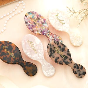 Peut inclure: Cinq brosses à cheveux personnalisées avec différents motifs et couleurs. Une brosse a un motif écaille de tortue, une autre un imprimé léopard, et les autres sont blanches et multicolores. Chaque brosse est gravée d'un nom en lettres dorées.