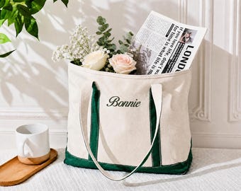 May include: A cream-colored canvas tote bag with dark green trim and handles. The name Bonnie is embroidered in black script on the front. The bag is filled with white and pink roses, greenery, and a newspaper with the visible text LONDON.