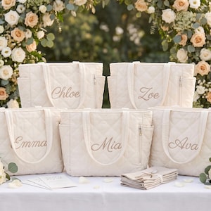 Pode incluir: Cinco sacos tote acolchoados em branco sujo com alças duplas e bolsos laterais. Cada saco apresenta um nome único bordado em letra cursiva: Chloe, Zoe, Emma, Mia e Ava. Os sacos têm um padrão de diamante e fechos de correr prateados.
