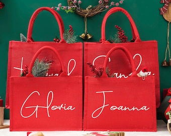 Könnte beinhalten: Zwei rote, rechteckige Tragetaschen mit stabilen Henkeln. Auf der Vorderseite der linken Tasche steht der Name Gloria in weißer Schreibschrift, auf der rechten Tasche der Name Joanna in weißer Schreibschrift. Beide Taschen haben eine Textilstruktur.