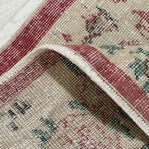 Puede incluir: Primer plano de una alfombra tejida con un borde rojo y blanco y un fondo beige con un patrón verde y rojo.