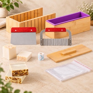 May include: A soap making kit featuring a bamboo loaf mold with a purple silicone liner, a bamboo cutting box, a stainless steel straight cutter, a wavy cutter with a red handle, a wooden lid, soap bars, a small roll of labels, and plastic bags.