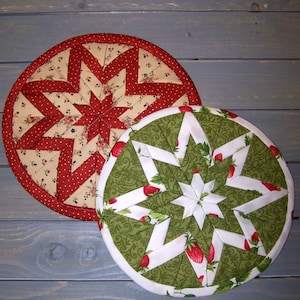 May include: Two round quilted pot holders. One is red and white with a starburst pattern. The other is green and white with a starburst pattern and strawberries.