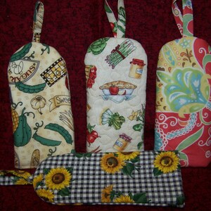 Puede incluir: Cuatro agarraderas de olla coloridas con diferentes patrones. Una tiene un patrón a cuadros con girasoles, otra tiene un patrón floral con acentos verdes y rojos, una tiene un patrón con verduras y el texto "Sweet Sugar", y otra tiene un patrón con verduras y una tarta.