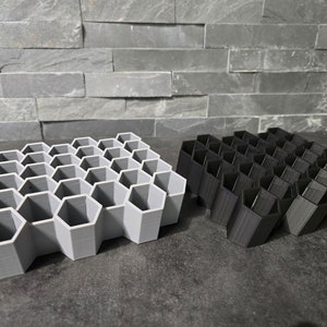 May include: Two honeycomb-shaped organizers, one gray and one black, made of plastic. The organizers are made up of hexagonal compartments.
