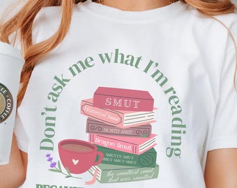 May include: White t-shirt with a graphic of stacked books, a coffee cup, and the text "Don't ask me what I'm reading because I will tell you." The books have titles like "SMUT" and "Dragon Smut."