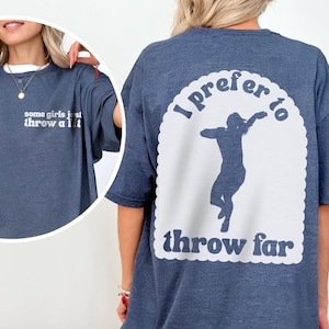 May include: A navy blue t-shirt with the text "some girls just throw a lit" on the front and "I prefer to throw far" with a silhouette of a person throwing on the back. The shirt has a white scalloped design around the back graphic.