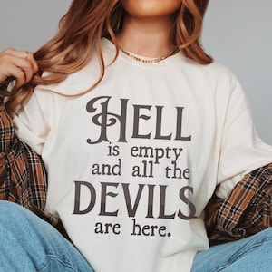 Puede incluir: Una camiseta blanca de manga larga con el texto "HELL is empty and all the DEVILS are here." impreso en negro.