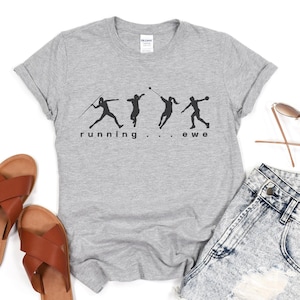 May include: A heather gray t-shirt with a black graphic of four track and field athletes in motion. The text "running . . . ewe" is printed below the figures. The image also includes brown leather sandals and denim shorts.