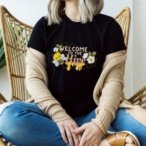 May include: A black t-shirt with a graphic of a cartoon bee and honeycomb with the text "Welcome to the Hive".