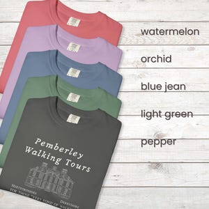 Op de afbeelding: Een stapel van vijf t-shirts in verschillende kleuren: watermeloen, orchidee, spijkerbroekblauw, lichtgroen en peper. Het onderste shirt heeft de tekst "Pemberley Walking Tours" en een illustratie van een gebouw.
