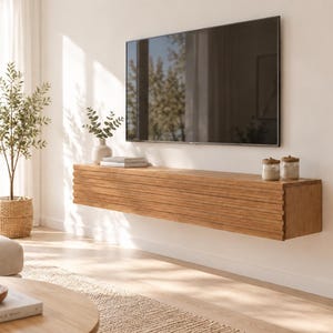 Könnte beinhalten: Ein langes, rechteckiges, wandmontiertes schwebendes Medienboard aus hellbraunem Holz mit horizontaler Lamellenstruktur. Das Board ist direkt unter einem großen Flachbildfernseher an einer weißen Wand angebracht.