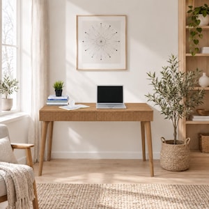 May include: A rectangular wooden desk with a fluted front drawer panel and four tapered legs. A silver laptop, a white mug, and a stack of books are placed on the surface. The desk is positioned in a room with a framed geometric print on the wall.