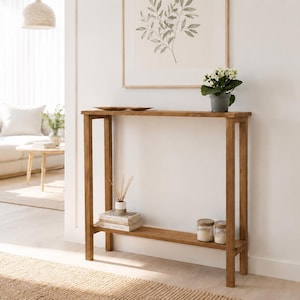 Peut inclure: Une console rectangulaire haute et étroite en bois de ton moyen. La table présente quatre pieds droits, une surface supérieure plate et une étagère inférieure unique positionnée près du sol. Le design est simple avec des lignes épurées.