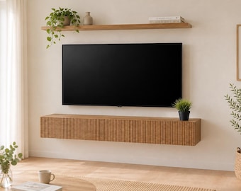 May include: A wall-mounted floating media console featuring a light brown wood finish with vertical slats across the front. The rectangular unit is positioned directly beneath a large flat-screen television and a single wooden shelf.