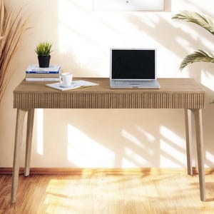 Può includere: Una scrivania in legno chiaro con un computer portatile, libri e una tazza di caffè sopra. La scrivania ha un design scanalato unico sul bordo anteriore ed è sostenuta da quattro gambe sottili.