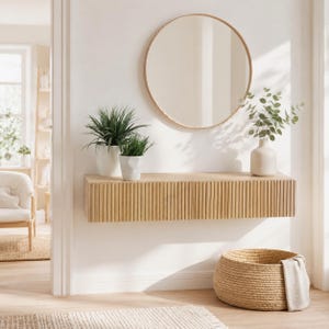 Può includere: Una mensola galleggiante in legno chiaro con scanalature verticali, che ospita due piante in vaso e un piccolo vaso con verde. Uno specchio rotondo con cornice in legno chiaro è appeso sopra la mensola. Un cesto intrecciato e un tappeto sono sul pavimento.