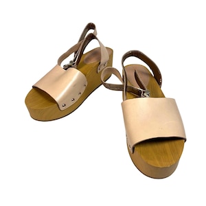 May include: A pair of light tan leather sandals with wooden platform soles. The sandals have a strap that goes around the ankle and a strap across the top of the foot. The soles are approximately 3 inches high.