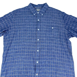 May include: Blue button-down shirt with a plaid pattern. The shirt has a button-down collar, a chest pocket, and short sleeves. The shirt is made of a lightweight fabric.