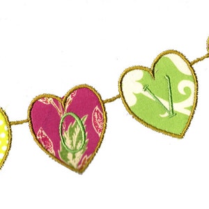 Può includere: Uno striscione di stoffa con la parola "LOVE" scritta in cuori colorati. Ogni cuore ha un motivo e un colore diverso, tra cui rosa, verde, giallo e viola.