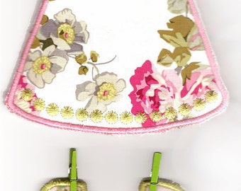 May include: Two fabric appliques of dresses with floral patterns. The top dress is white with pink trim and a green floral pattern. The bottom dress is white with a green trim and a yellow floral pattern.