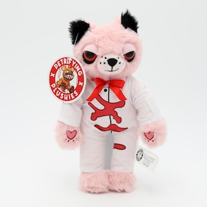 May include: Pink plush teddy bear with black ears and a white outfit. The bear has red eyes and a red bow tie. The bear is wearing a white shirt with a red bone design and white pants. The bear is holding a knife in its right paw. The bear is standing on a white background. The bear has a tag that says "Detrifying Plushies x Crazy Cat".