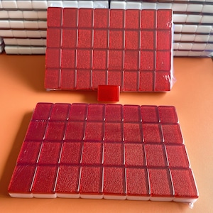 May include: Two sets of red mahjong tiles with white edges. The tiles are arranged in a rectangular shape and are wrapped in plastic.