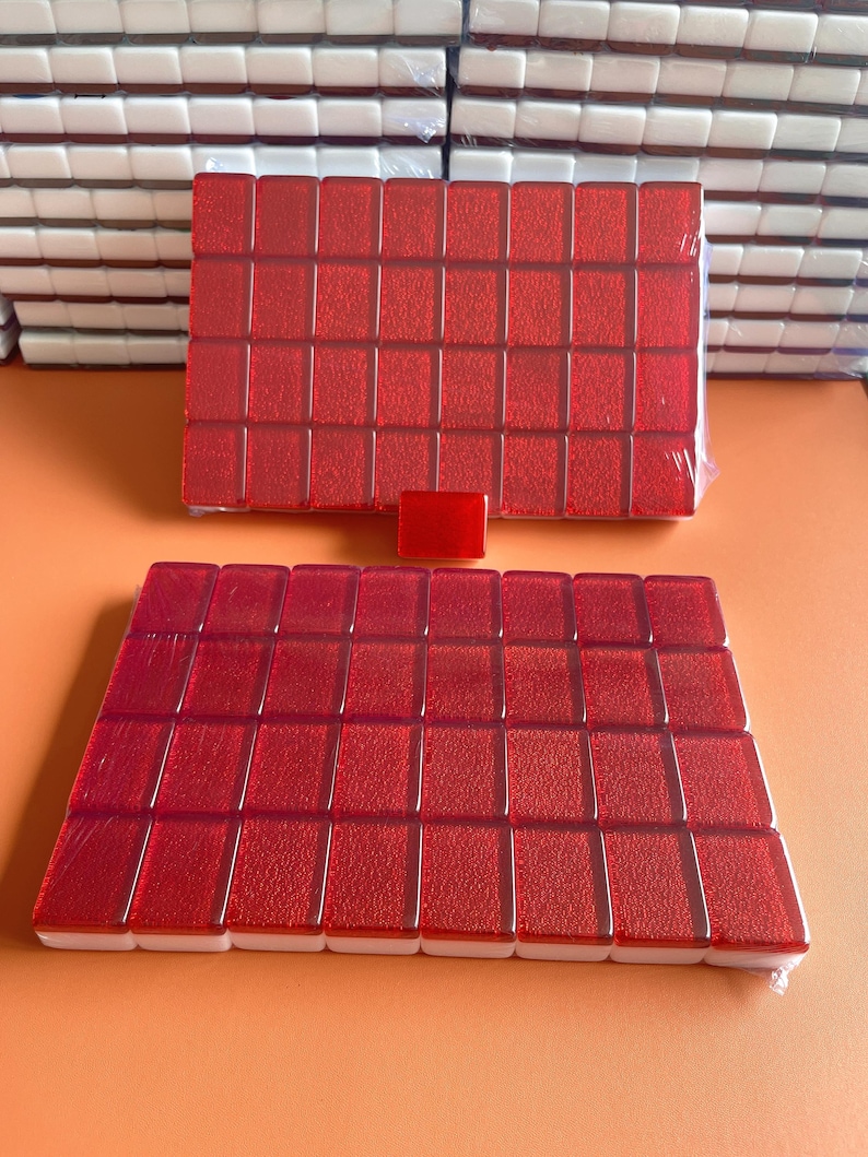 May include: Two sets of red mahjong tiles with white edges. The tiles are arranged in a rectangular shape and are wrapped in plastic.
