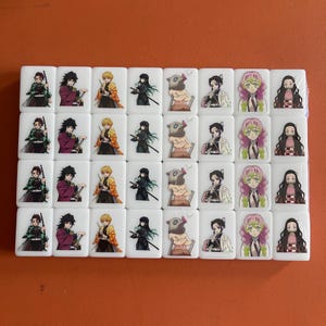 May include: A set of white tiles featuring colorful anime character illustrations. Each tile displays a different character, with a variety of poses and outfits. The tiles are arranged in a rectangular pattern.