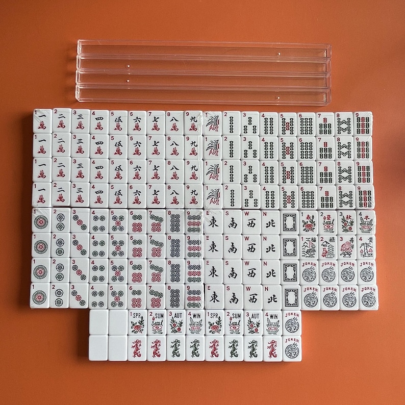 May include: A set of white mahjong tiles with red and black markings. The tiles are arranged in a grid pattern and include numbers, symbols, and characters. The tiles are on a brown surface.