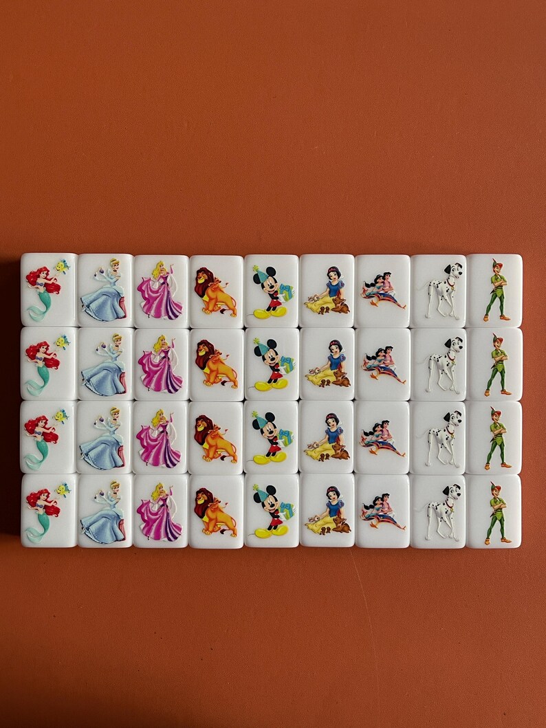 May include: A set of 36 white dominoes featuring colourful Disney character illustrations. The characters include Ariel, Cinderella, Snow White, Mickey Mouse, Simba, and Peter Pan.