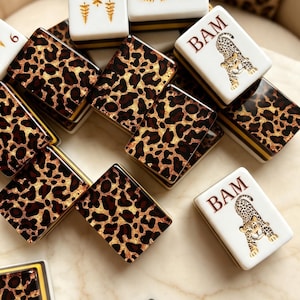 May include: A collection of rectangular mahjong tiles featuring a mix of designs. Some tiles display a brown and black leopard print pattern, while others are white with gold tree illustrations or a leopard graphic with the text BAM.