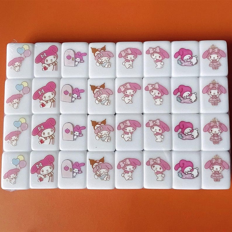 Puede incluir: Un juego de 36 fichas de mahjong blancas con im&aacute;genes coloridas de Hello Kitty y sus amigos. Las fichas presentan varios dise&ntilde;os, incluyendo Hello Kitty sosteniendo un globo, Hello Kitty sosteniendo una puerta, Hello Kitty sosteniendo un regalo y Hello Kitty con una corona.