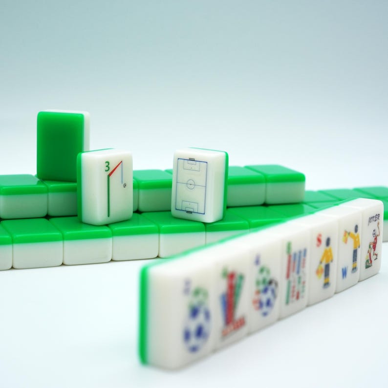 Puede incluir: Un conjunto de fichas de mahjong blancas y verdes dispuestas en filas. Algunas fichas presentan gr&aacute;ficos con tem&aacute;tica de f&uacute;tbol, incluyendo un campo, el n&uacute;mero tres con una porter&iacute;a y varias figuras de jugadores. Forma rectangular.