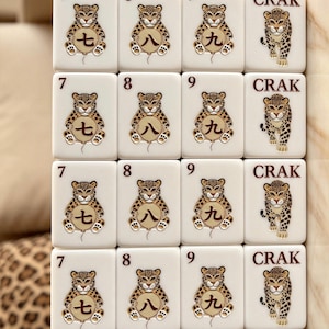 May include: A set of sixteen white rectangular mahjong tiles arranged in a four-by-four grid. Each tile features a leopard illustration. The tiles display the numbers 7, 8, 9, and the text CRAK, accompanied by Chinese characters on balloons.