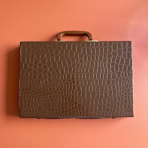 May include: A brown leather briefcase with a crocodile pattern and a gold handle.