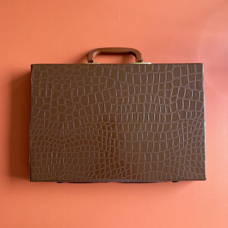 May include: A brown leather briefcase with a crocodile pattern and a gold handle.