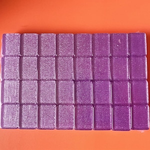 May include: A sheet of purple glitter tiles. The tiles are arranged in a grid pattern and have a shimmery finish.