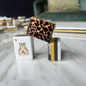 May include: Three mahjong tiles arranged in a stack. One tile features a white face with the number 9 and a leopard illustration with a Chinese character. Another tile displays a brown and black leopard print pattern. The third tile shows side stripes.