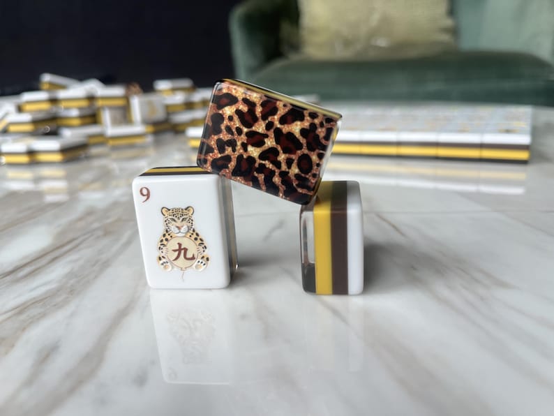May include: Three mahjong tiles arranged in a stack. One tile features a white face with the number 9 and a leopard illustration with a Chinese character. Another tile displays a brown and black leopard print pattern. The third tile shows side stripes.