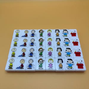 May include: A set of white mahjong tiles featuring cartoon characters. Each tile has a different character illustration in color. The tiles are arranged in rows on a light orange background.