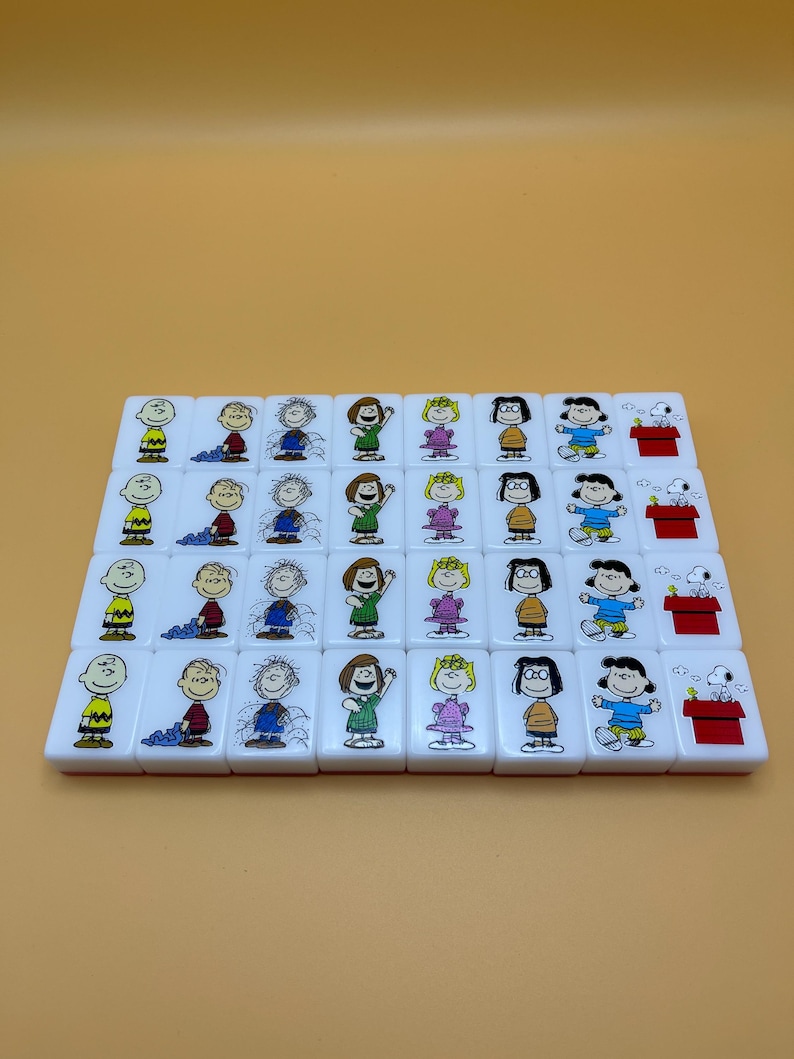May include: A set of white mahjong tiles featuring cartoon characters. Each tile has a different character illustration in color. The tiles are arranged in rows on a light orange background.