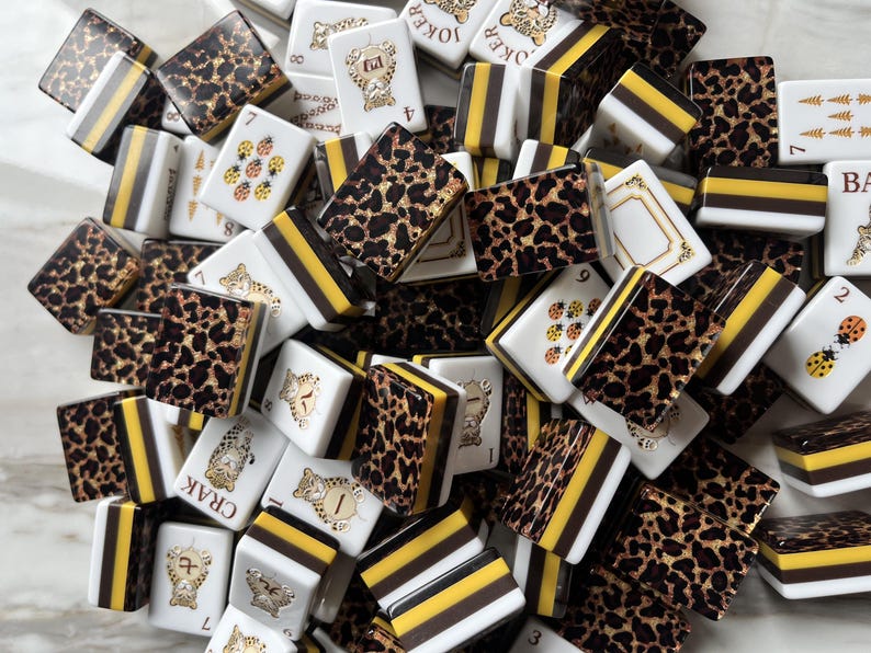 May include: A collection of rectangular mahjong tiles featuring a mix of designs, including leopard print patterns, yellow and black striped edges, and white tiles with illustrations of ladybugs, tigers, and the text Joker, Crak, and Ba.