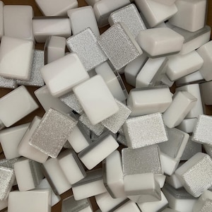 May include: A collection of rectangular mosaic tiles. Some tiles are solid white, while others have a textured, silver glitter finish. The tiles are scattered, creating a visually interesting pattern. These tiles are suitable for various craft and design projects.