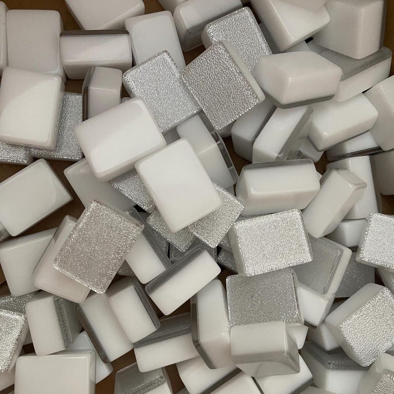 May include: A collection of rectangular mosaic tiles. Some tiles are solid white, while others have a textured, silver glitter finish. The tiles are scattered, creating a visually interesting pattern. These tiles are suitable for various craft and design projects.