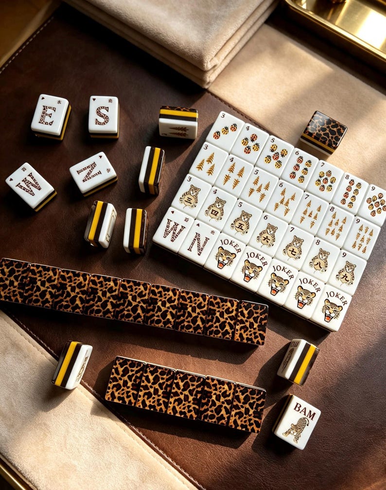 May include: A Mahjong set featuring white tiles with leopard print backs and sides with black and yellow stripes. The tiles display various illustrations including tigers, ladybugs, pine trees, and the word JOKER, along with letters E, S, M, Z, and BAM.