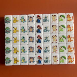 May include: A set of 36 white dominoes with colorful Pokemon characters printed on each side. The characters include Pikachu, Bulbasaur, Squirtle, Charmander, and more.