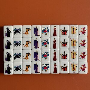 May include: A set of 24 white square tiles featuring various Disney villain characters. The characters include Maleficent, Ursula, Scar, Jafar, and Cruella de Vil.