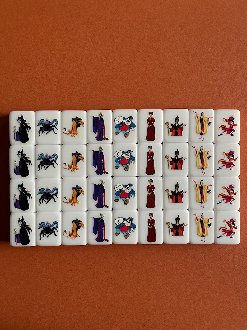 May include: A set of 24 white square tiles featuring various Disney villain characters. The characters include Maleficent, Ursula, Scar, Jafar, and Cruella de Vil.